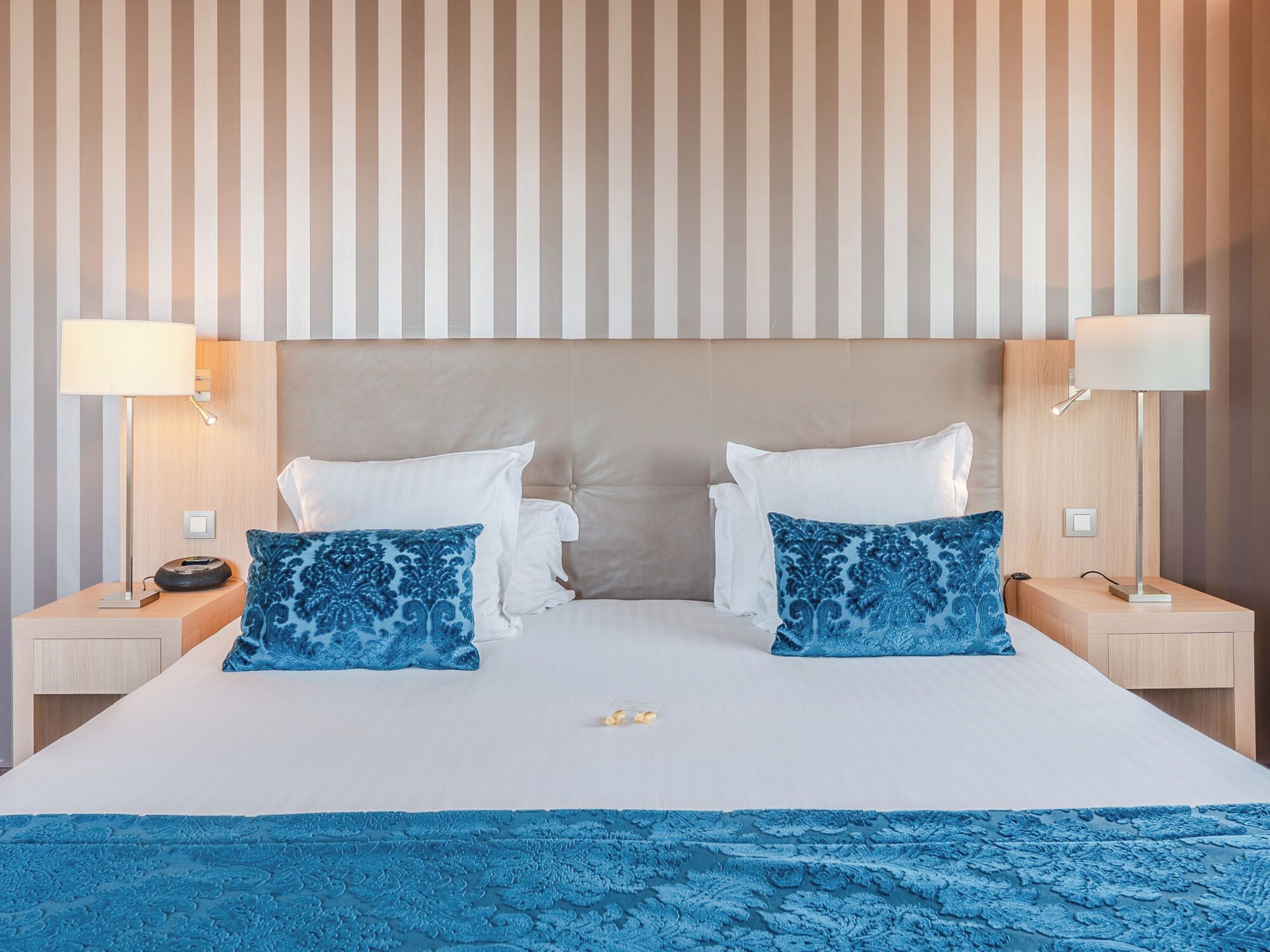 A hotel room with a large bed, two bedside tables, and a striped wall.