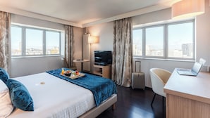 Quarto de hotel com cama, escrivaninha, cadeira, televisão e vista para a cidade.