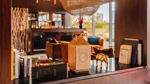 Um espaço de bar acolhedor, com uma luminária pendente de vime, um balcão de madeira com livros e um elefante decorativo, e uma área de estar confortável com um assento azul.