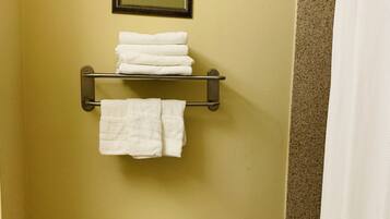 A bathroom with a toilet, a towel rack with folded towels, and a framed picture on the wall.