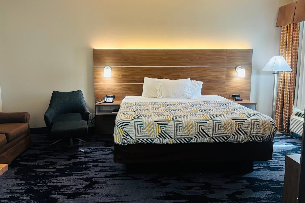 A hotel room with a large bed, a desk with a phone, a chair, and a lamp.