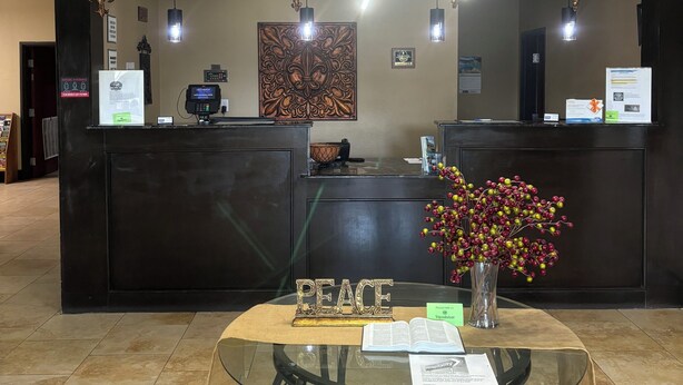Una recepción con un cartel que dice 'PEACE', un jarrón con flores y una mesa de vidrio con folletos.
