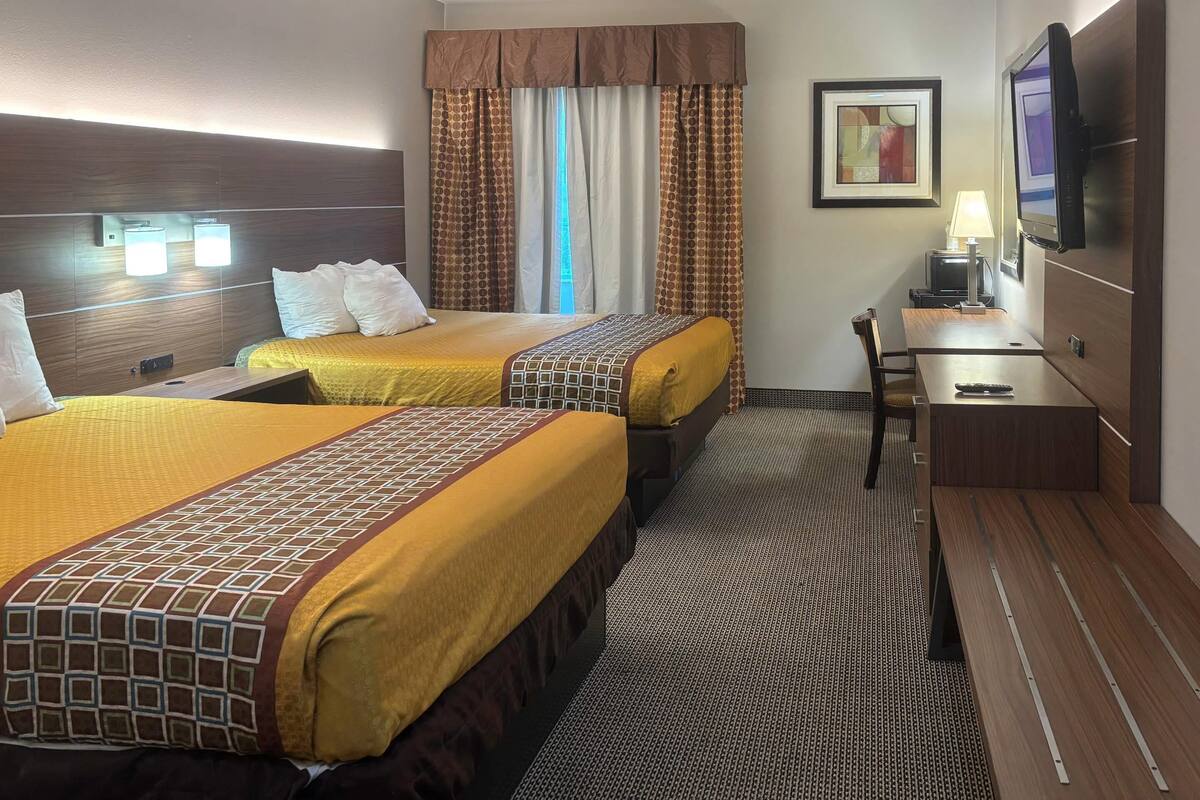 A hotel room with two beds, a desk, a television, and a window with curtains.
