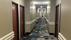 Un pasillo de hotel con alfombra estampada, puertas a ambos lados e iluminación en el techo.