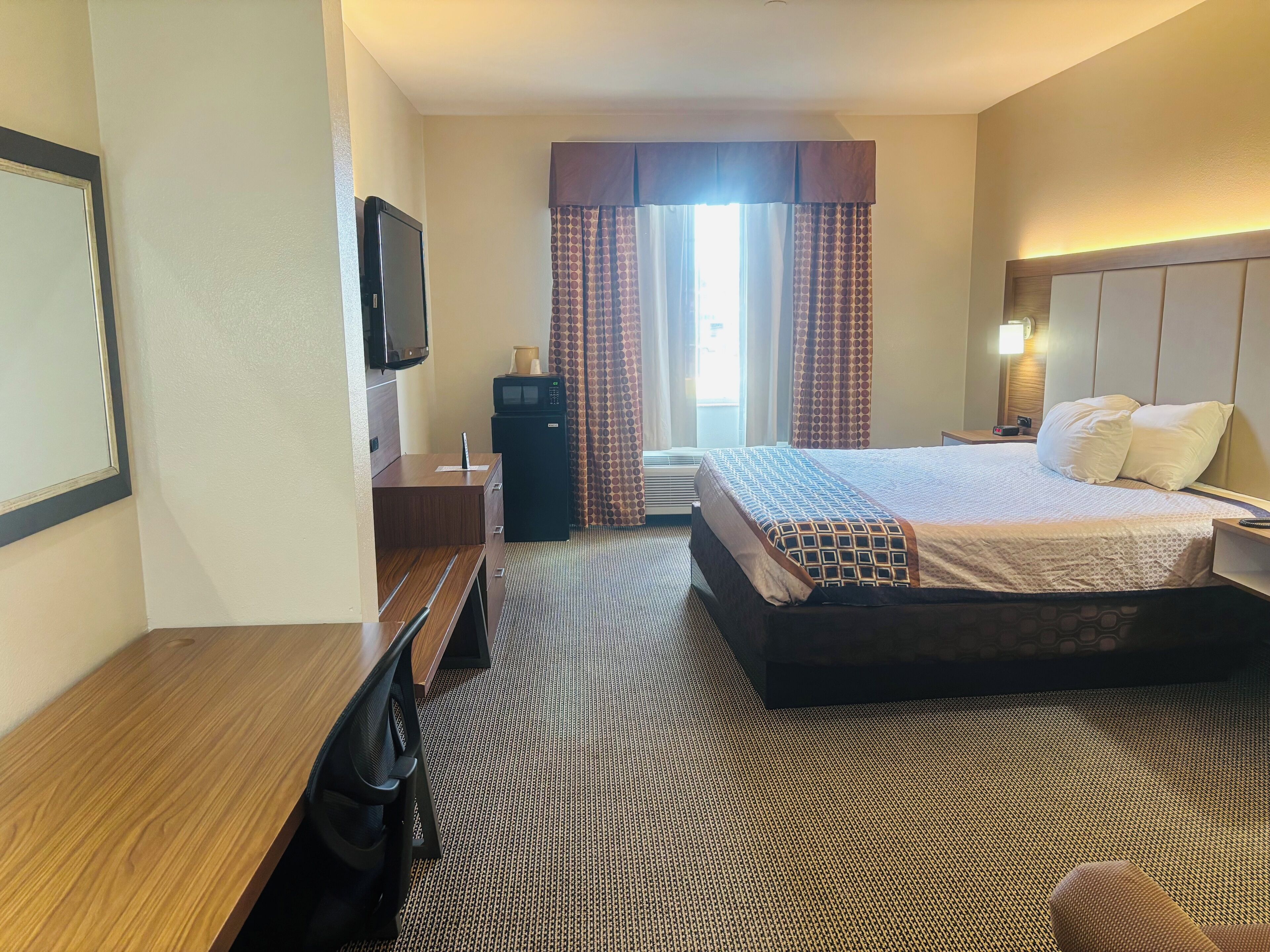 A hotel room with a bed, a desk, a television, a microwave, and a window with curtains.