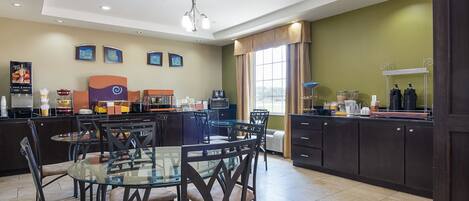 A modern kitchen with a dining area, featuring a glass table, dark wooden chairs, and a kitchen counter with various appliances.