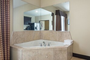 A bathroom with a large bathtub, a mirror, and a towel stack.
