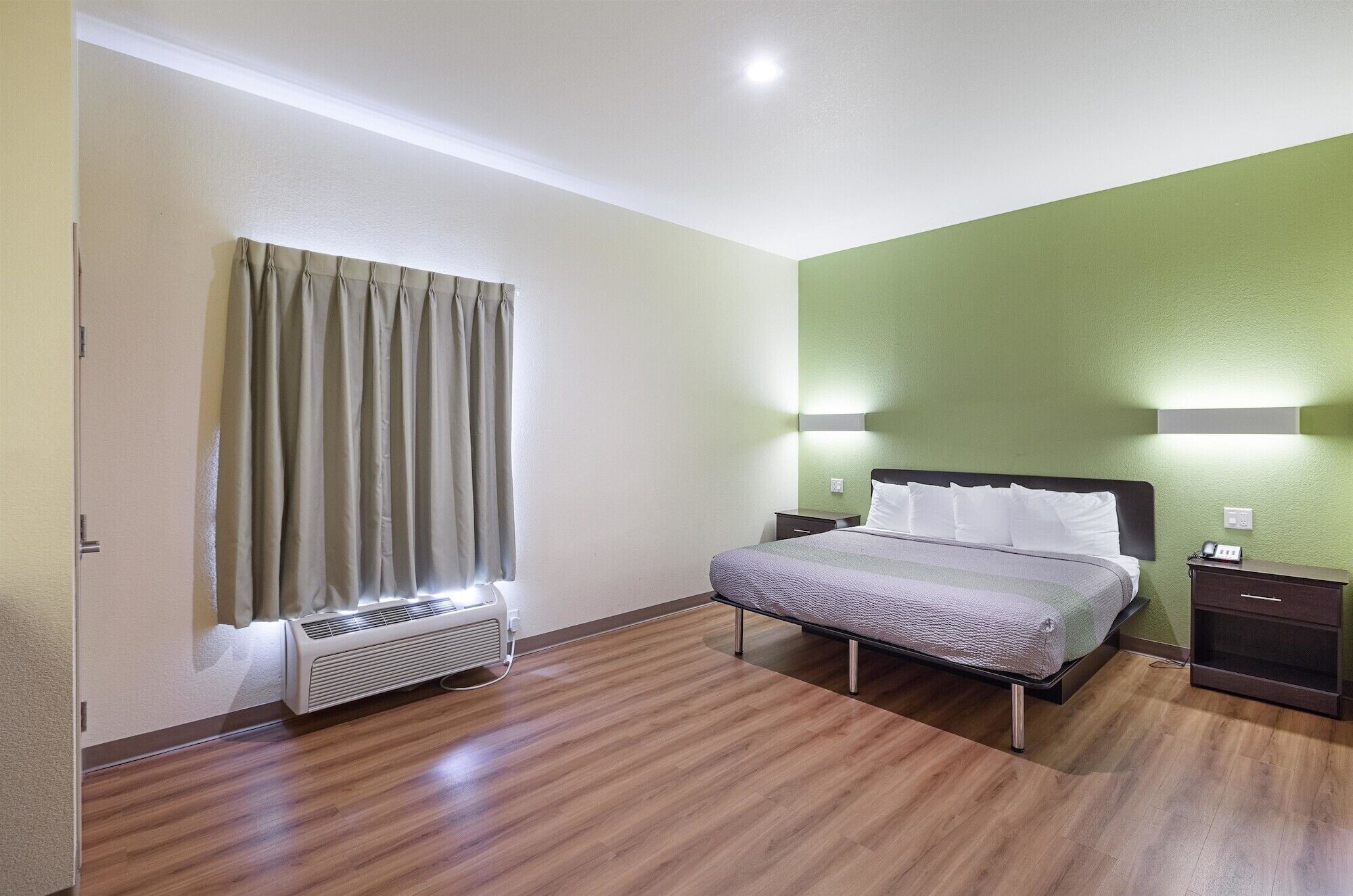 Una habitación de hotel con cama, mesitas de noche, un calefactor y una ventana con cortinas.