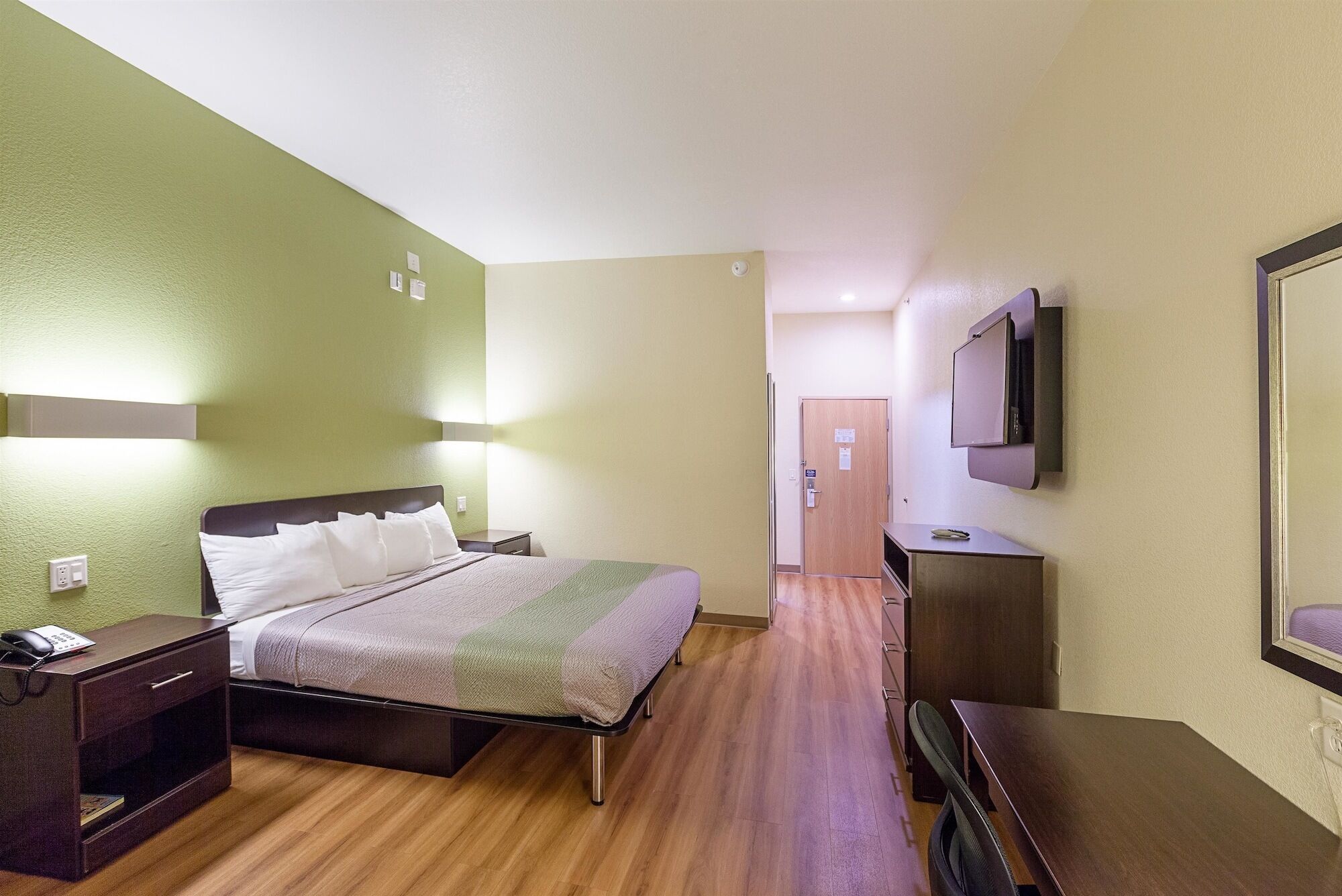A hotel room with a bed, bedside table, TV, and a desk.