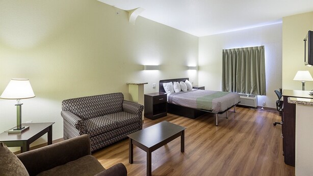 Quarto de hotel com cama, sofá, mesa pequena e escrivaninha. Há duas luminárias nas mesas de cabeceira e uma janela com cortinas.