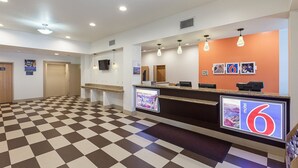 Uma área de recepção de hotel com piso xadrez, um balcão de atendimento e uma TV fixada na parede.