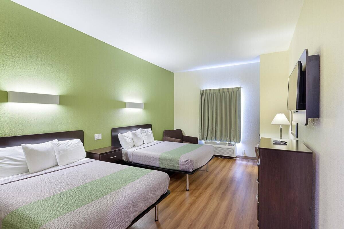 A hotel room with two beds, a desk, a chair, a TV, and a window with curtains.