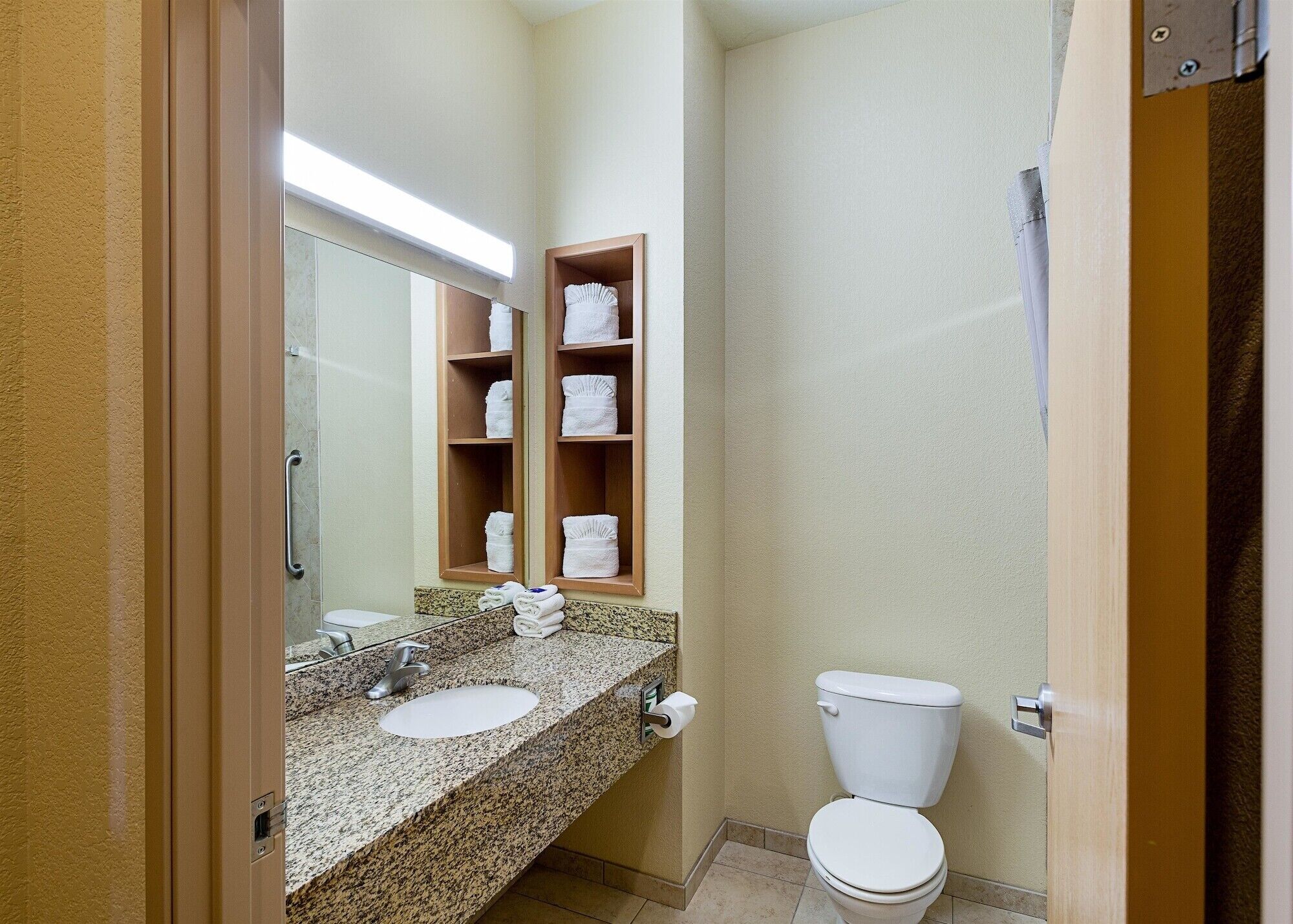 Un baño de hotel pequeño con encimera de granito, un lavabo, un inodoro y un espejo.