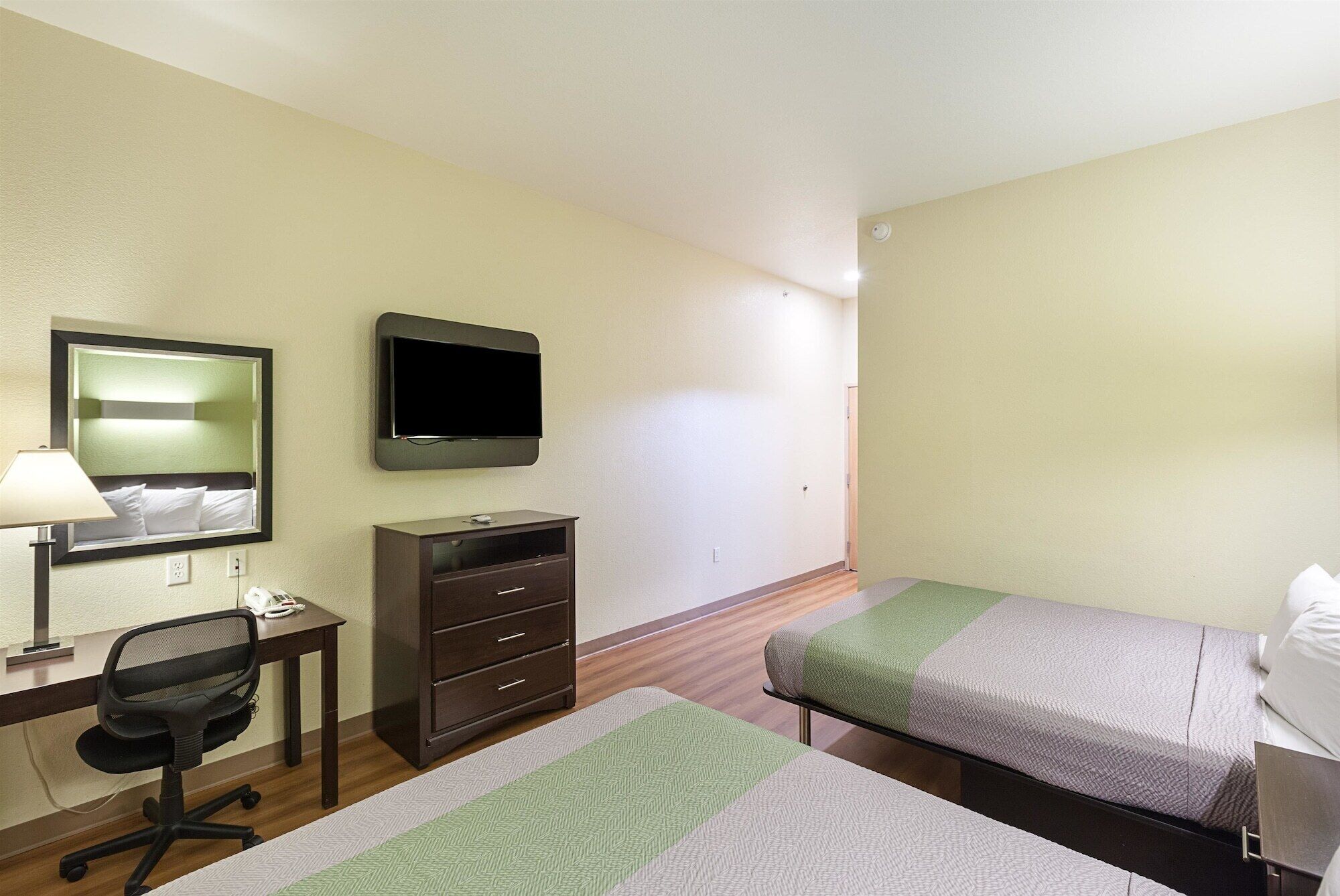 A hotel room with a desk, chair, two beds, a TV, and a dresser.