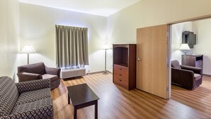 Quarto de hotel com sofá, mesinha, armário e televisão.