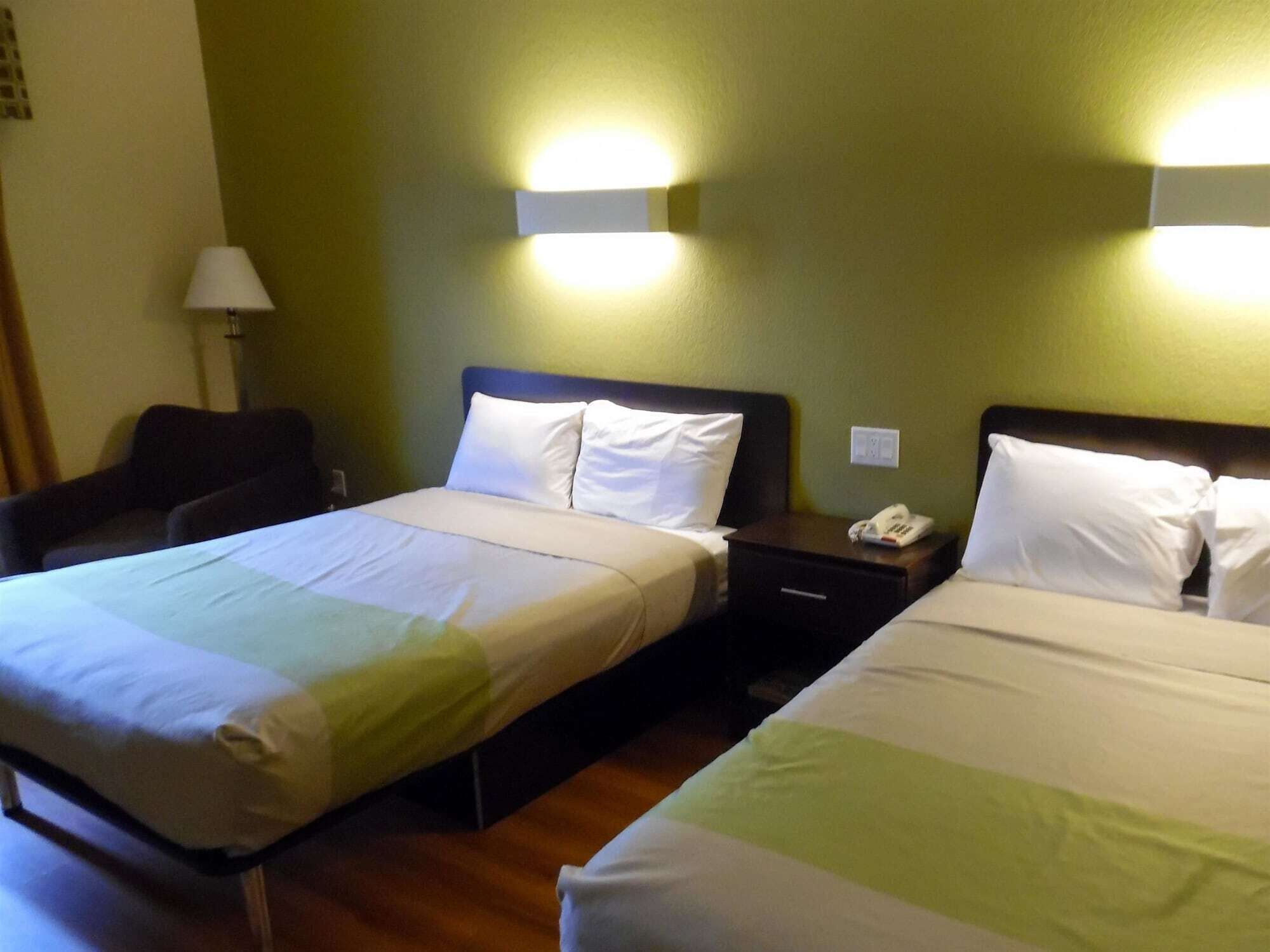 Habitación de hotel con dos camas, una mesita de noche con teléfono, una lámpara y una silla.