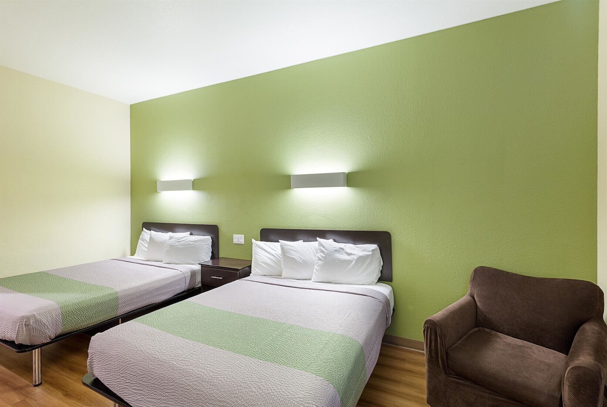 A hotel room with two beds, a brown armchair, and green walls.
