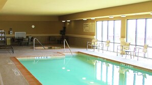 An indoor swimming pool with clear water, a lifeguard chair, and a seating area with chairs.