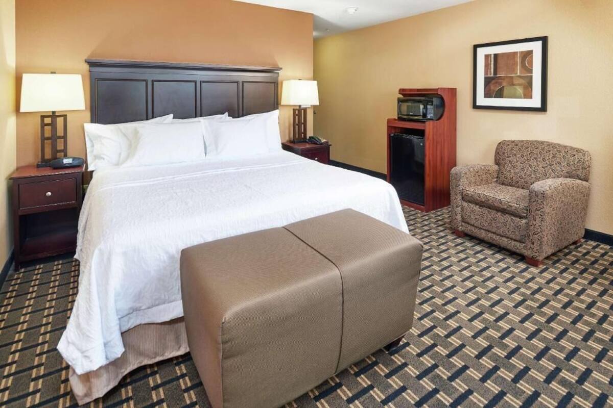 A hotel room with a bed, bedside tables, a chair, a microwave, and a framed picture on the wall.