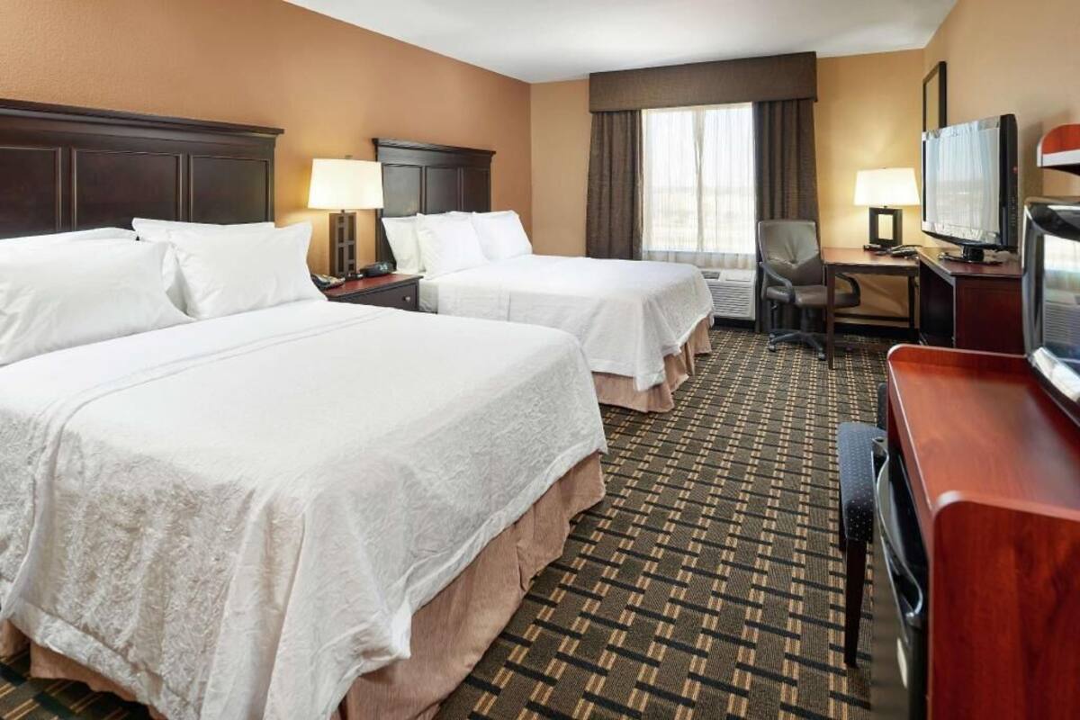 A hotel room with two beds, a TV, a desk, and a chair.