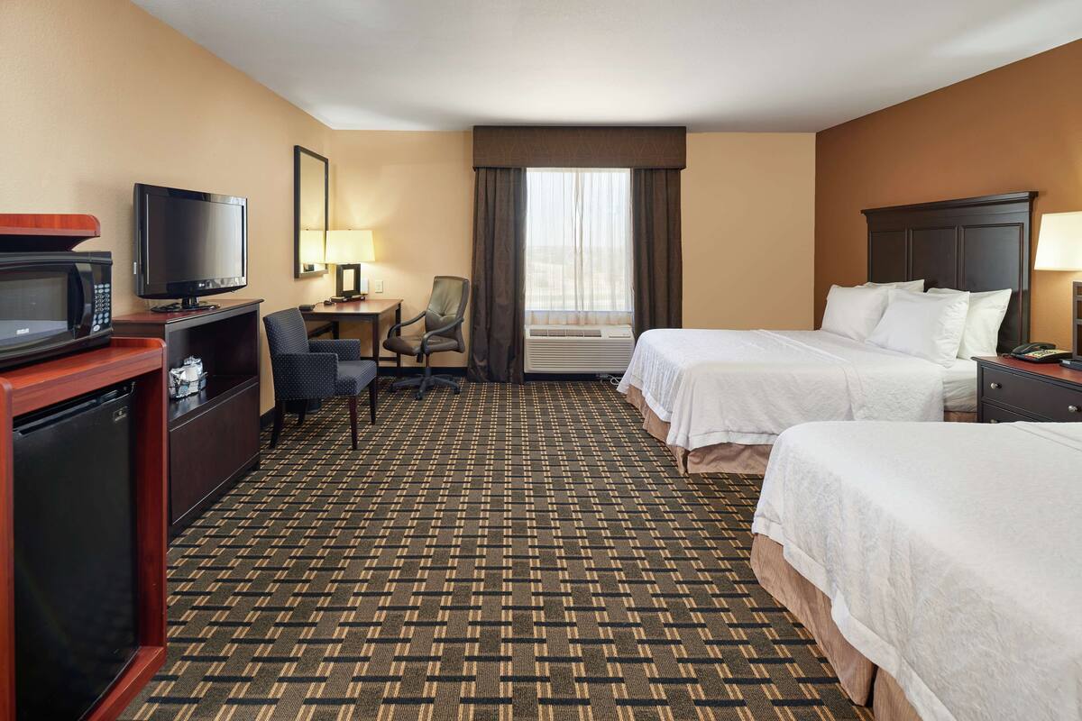 A hotel room with two beds, a television, a desk with a computer, and a microwave.