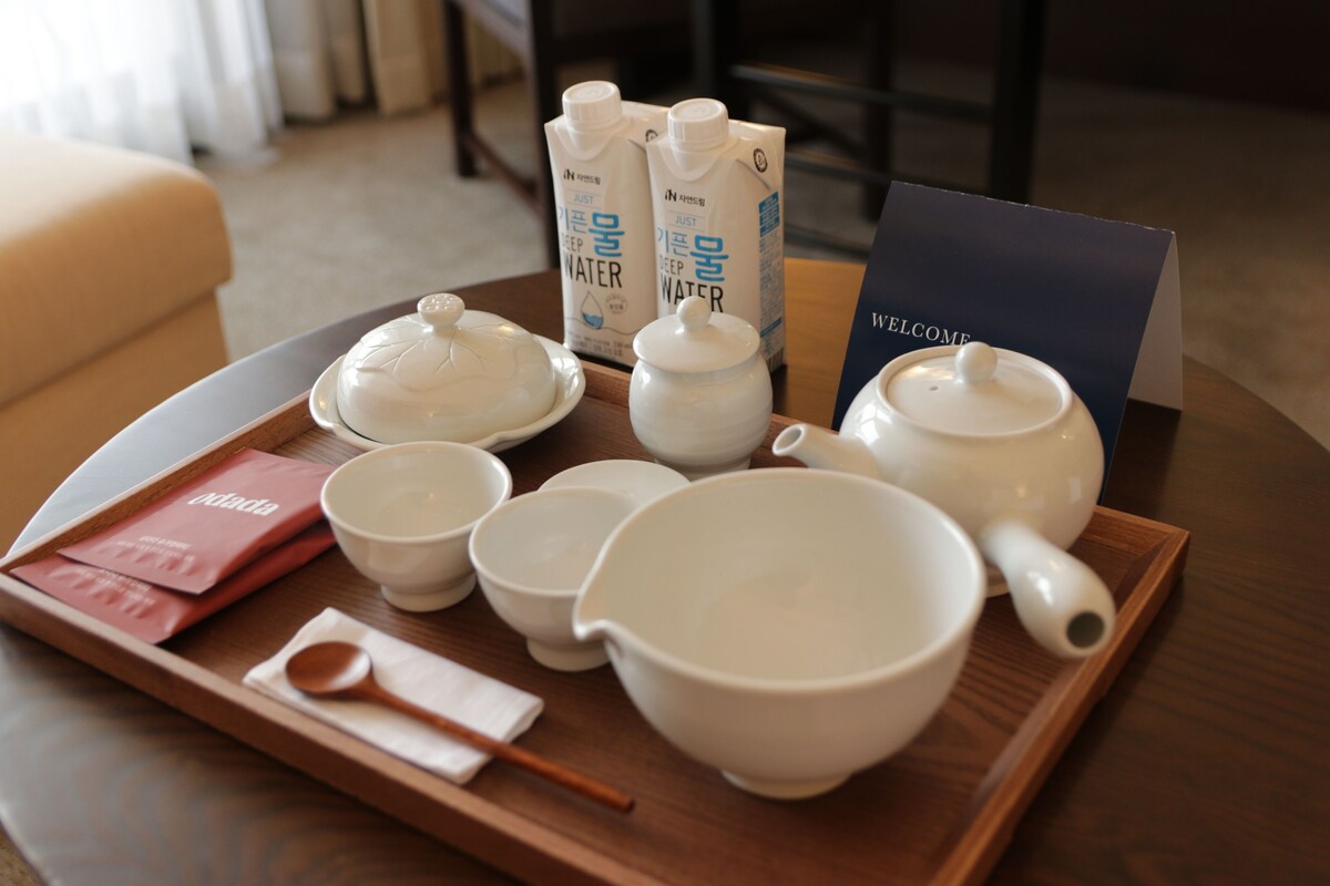 A tray with tea sets, a wooden spoon, and a welcome card on a table.