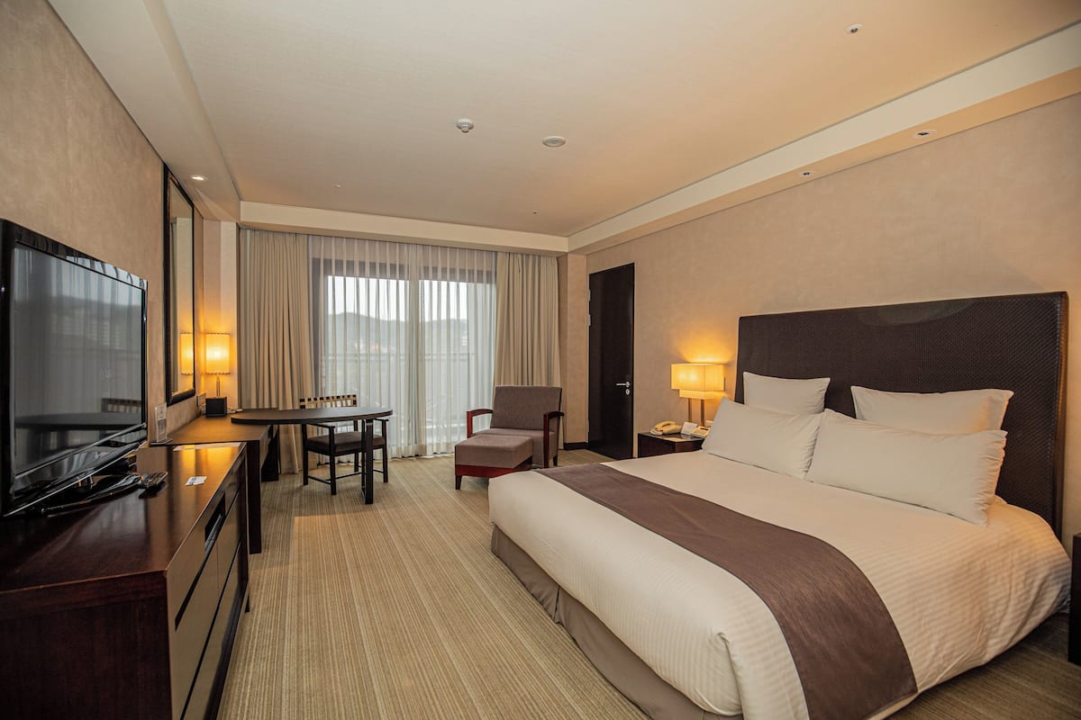 Una habitación de hotel con una cama grande, un escritorio con silla, televisión y ventana con cortinas.