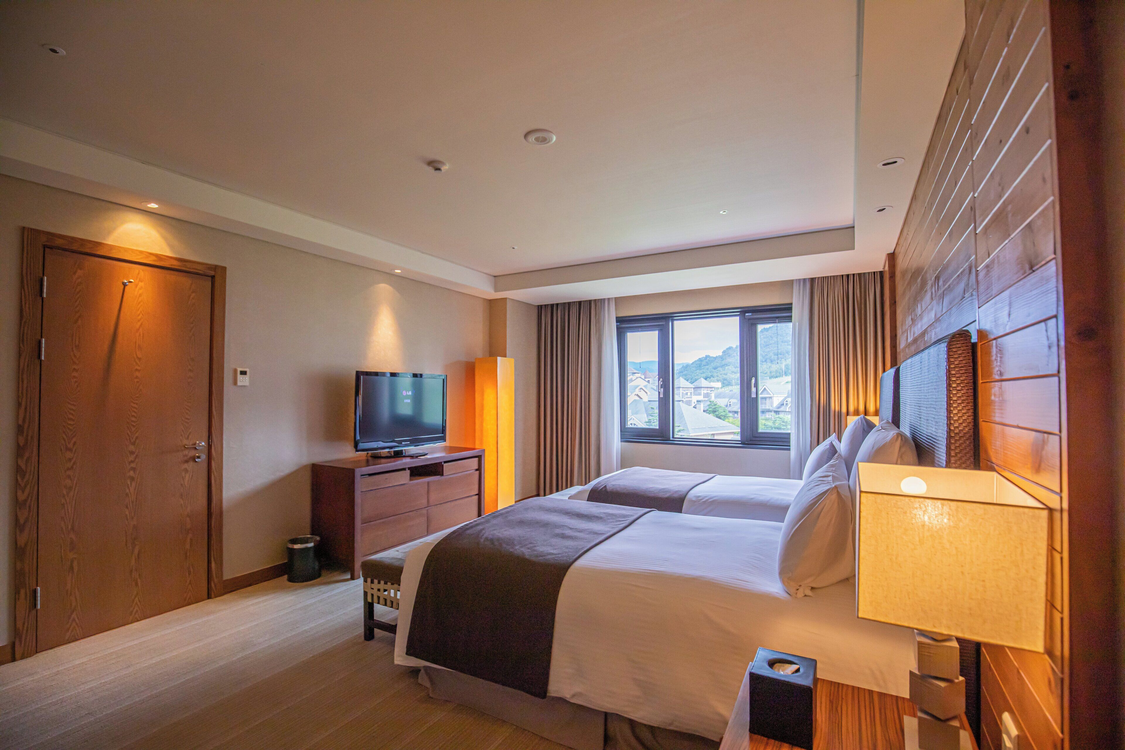 A hotel room with a large bed, a television, a window with a view, and wooden paneling.