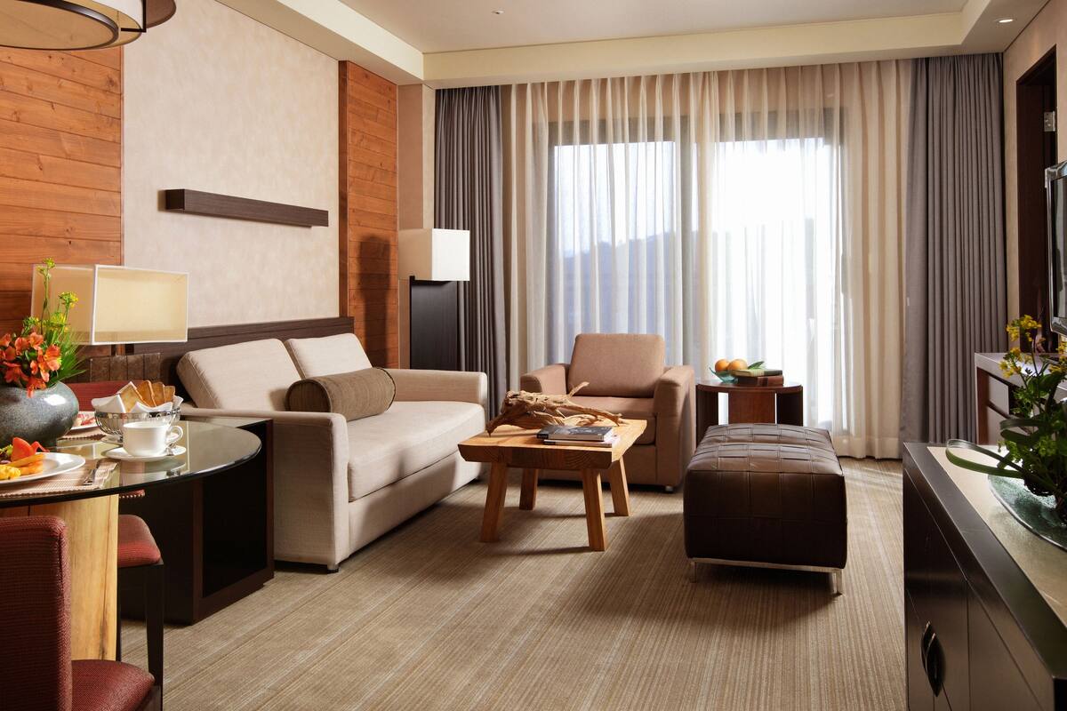 Una habitación de hotel moderna con sofá, sillón, mesa de centro y un área de comedor con mesa de vidrio.
