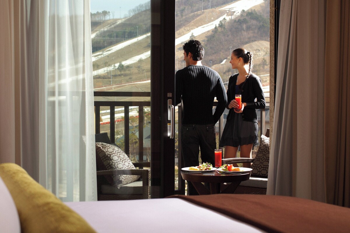 A hotel room with a balcony overlooking a mountainous landscape.