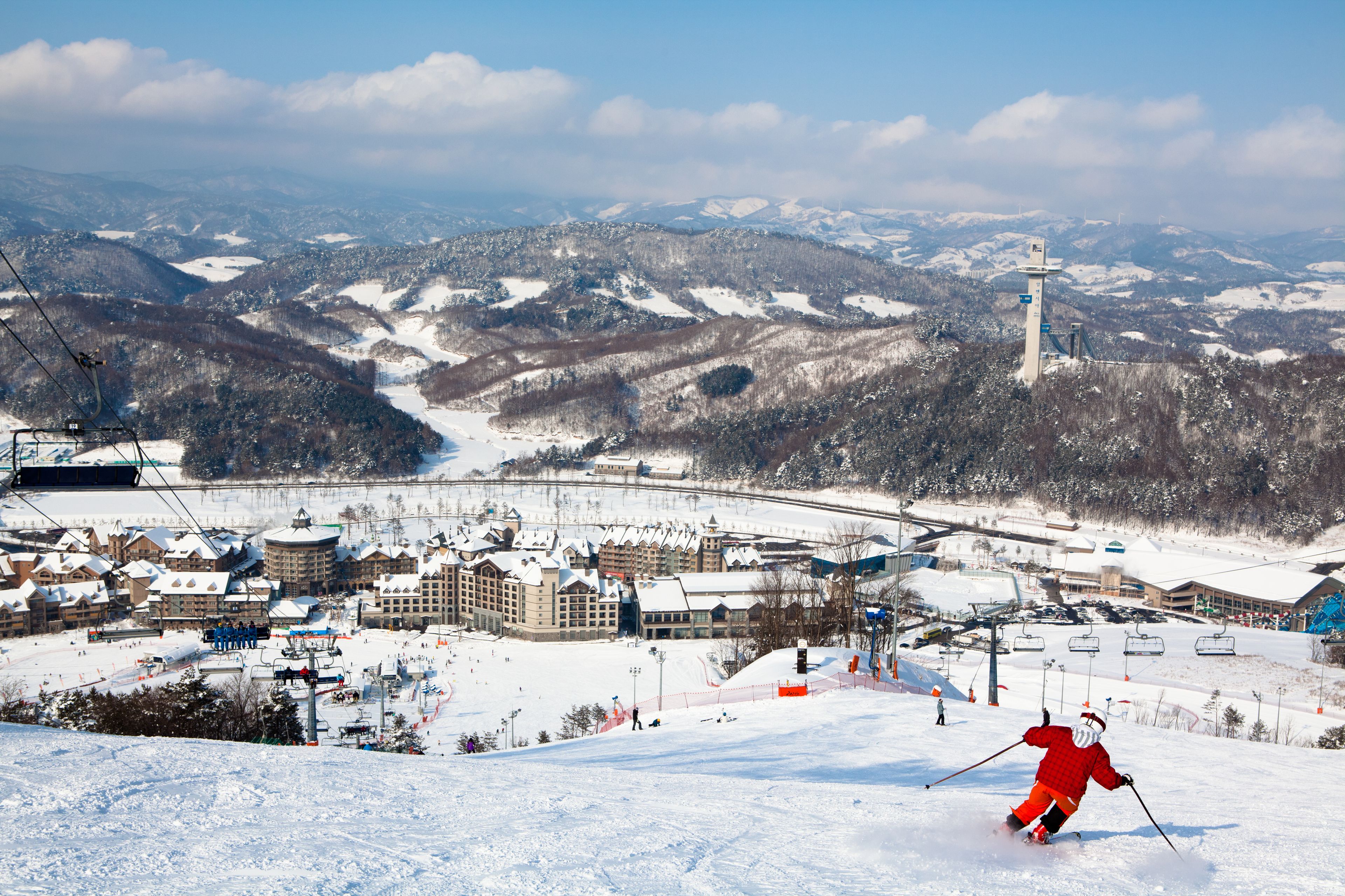 Une station de ski dotée d’un télésiège, de pistes enneigées et d’une ville dont les bâtiments se dessinent à l’arrière-plan.