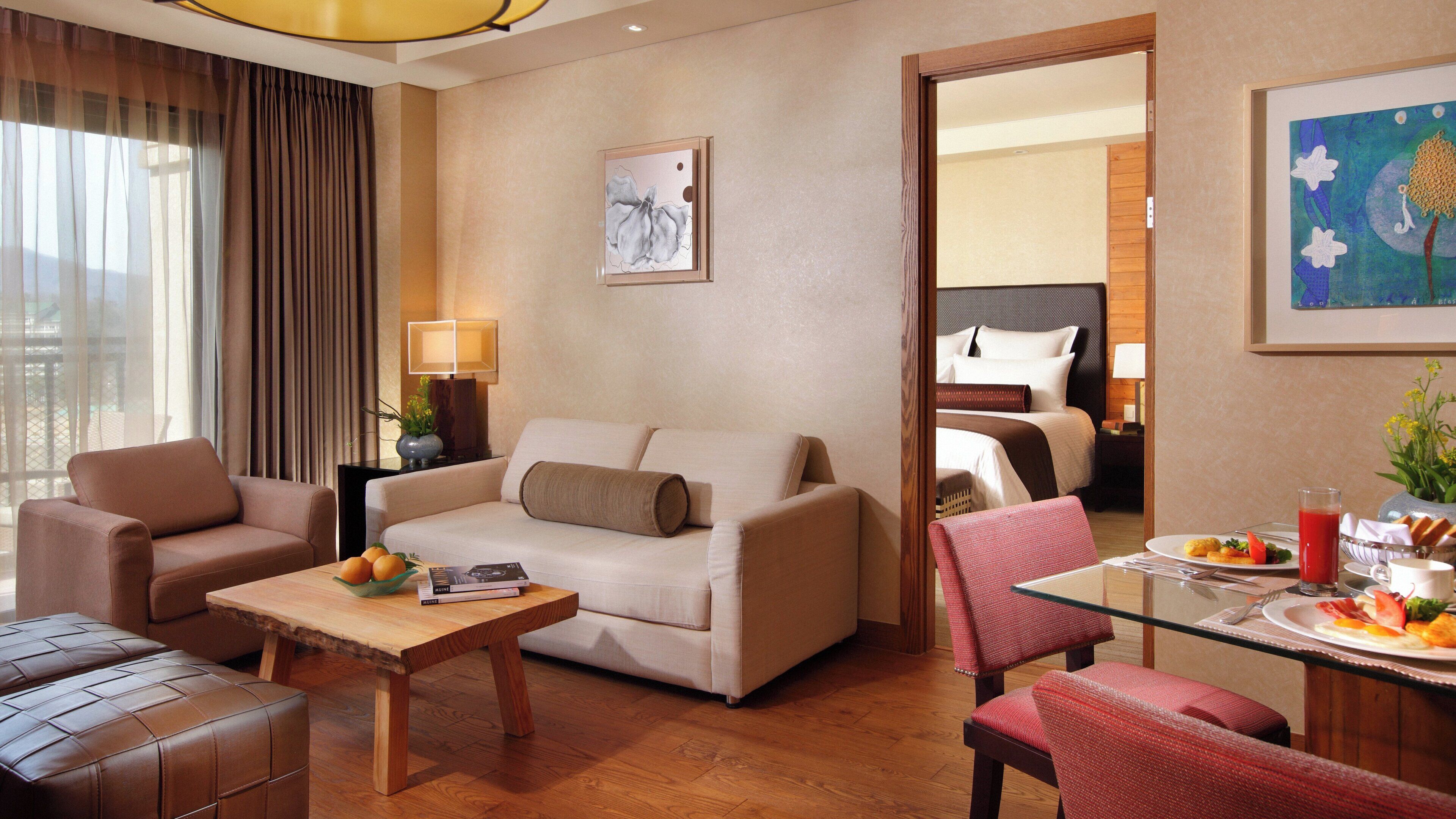 Une chambre d’hôtel avec un canapé, des fauteuils, une table à manger où le petit-déjeuner est servi, un lit et un tableau au mur.