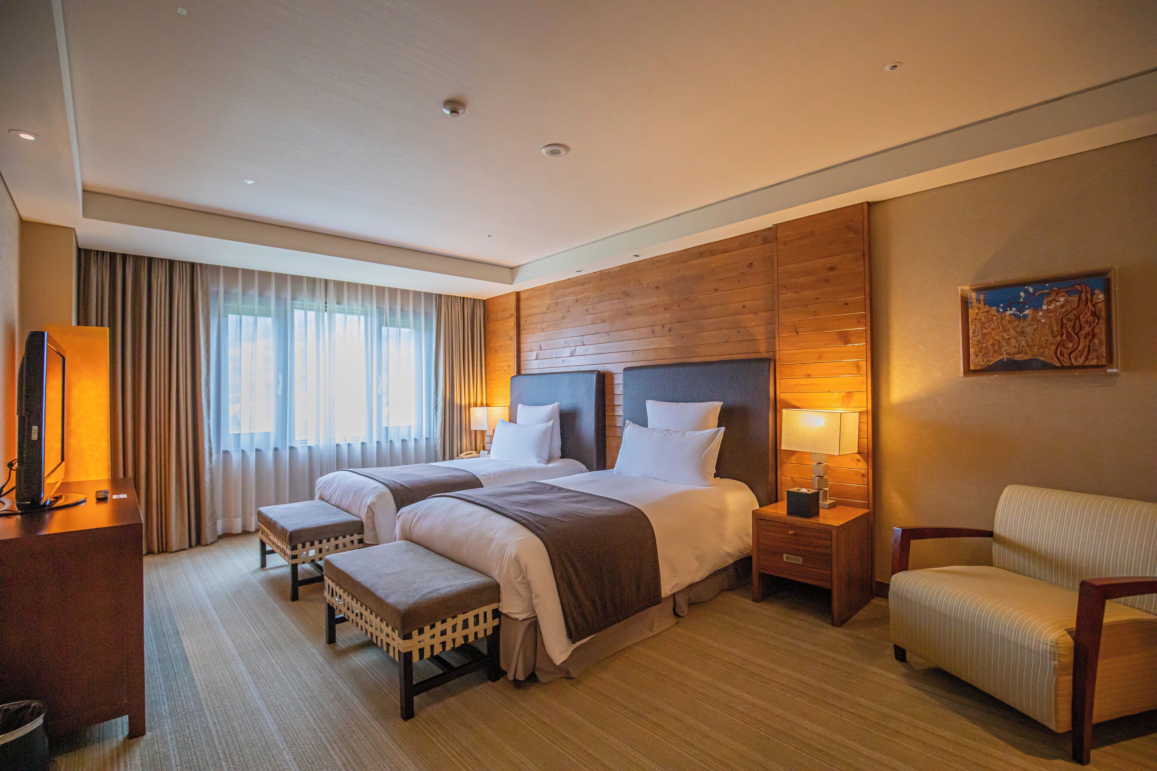 Een hotelkamer met twee bedden, een bureau, een stoel en een groot raam met gordijnen.