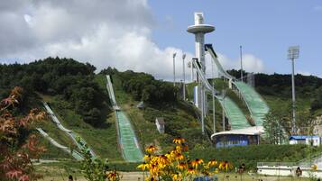 A ski lift system with multiple chairlifts and a central tower, surrounded by greenery and a clear sky.