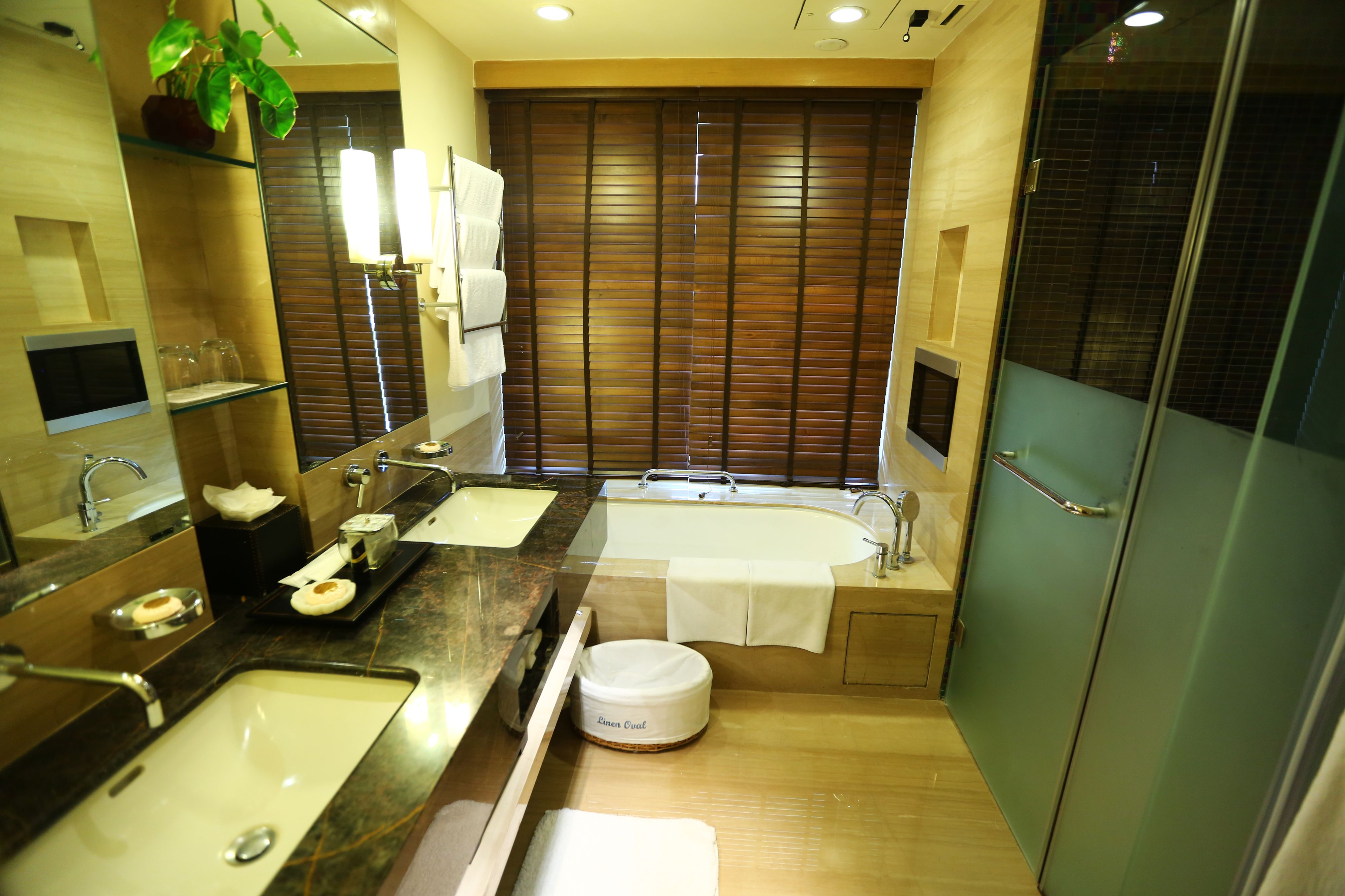 A modern bathroom with a large mirror, dual sinks, a bathtub, and a toilet.