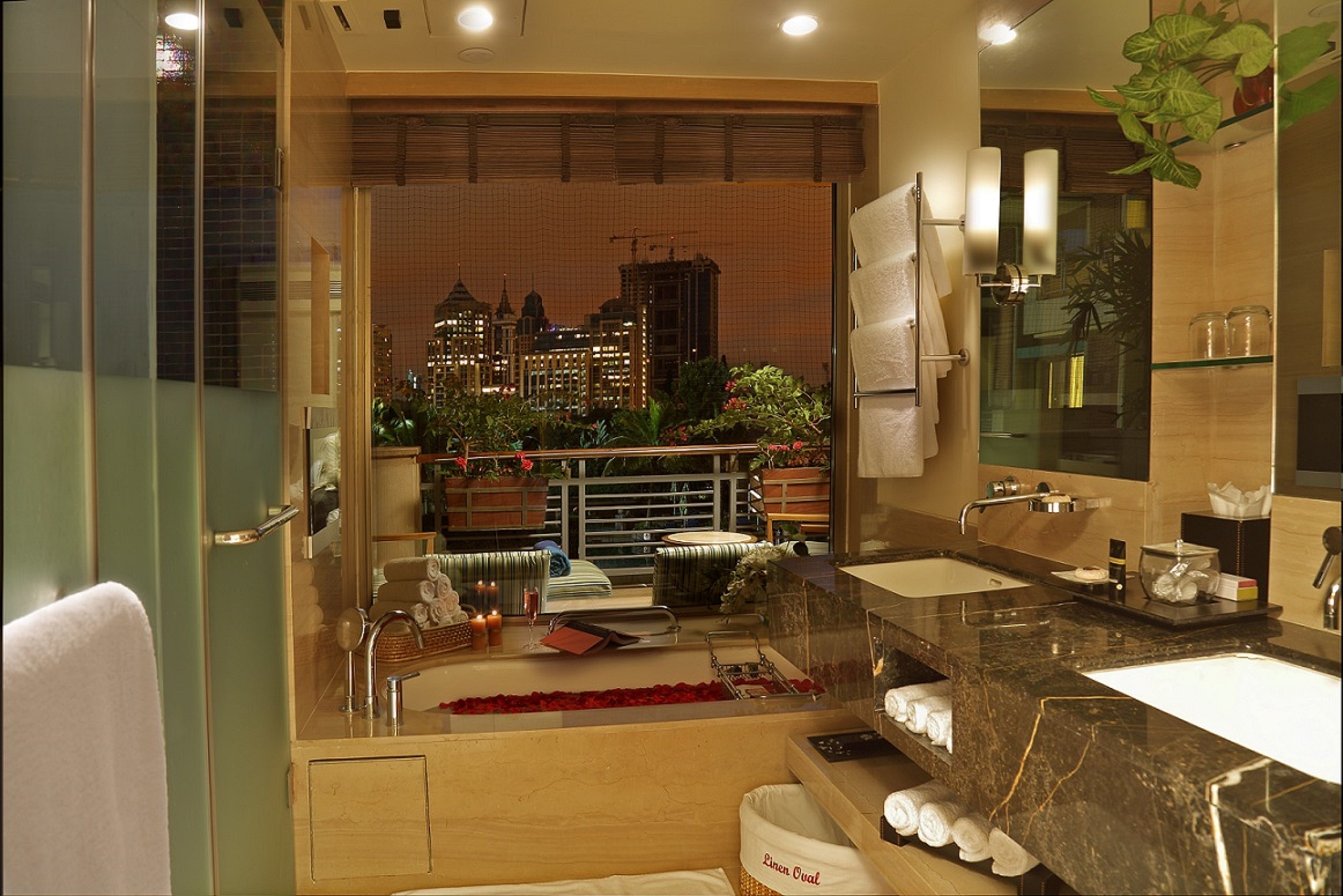 A modern bathroom with a large mirror, dual sinks, and a view of a cityscape through a glass door.