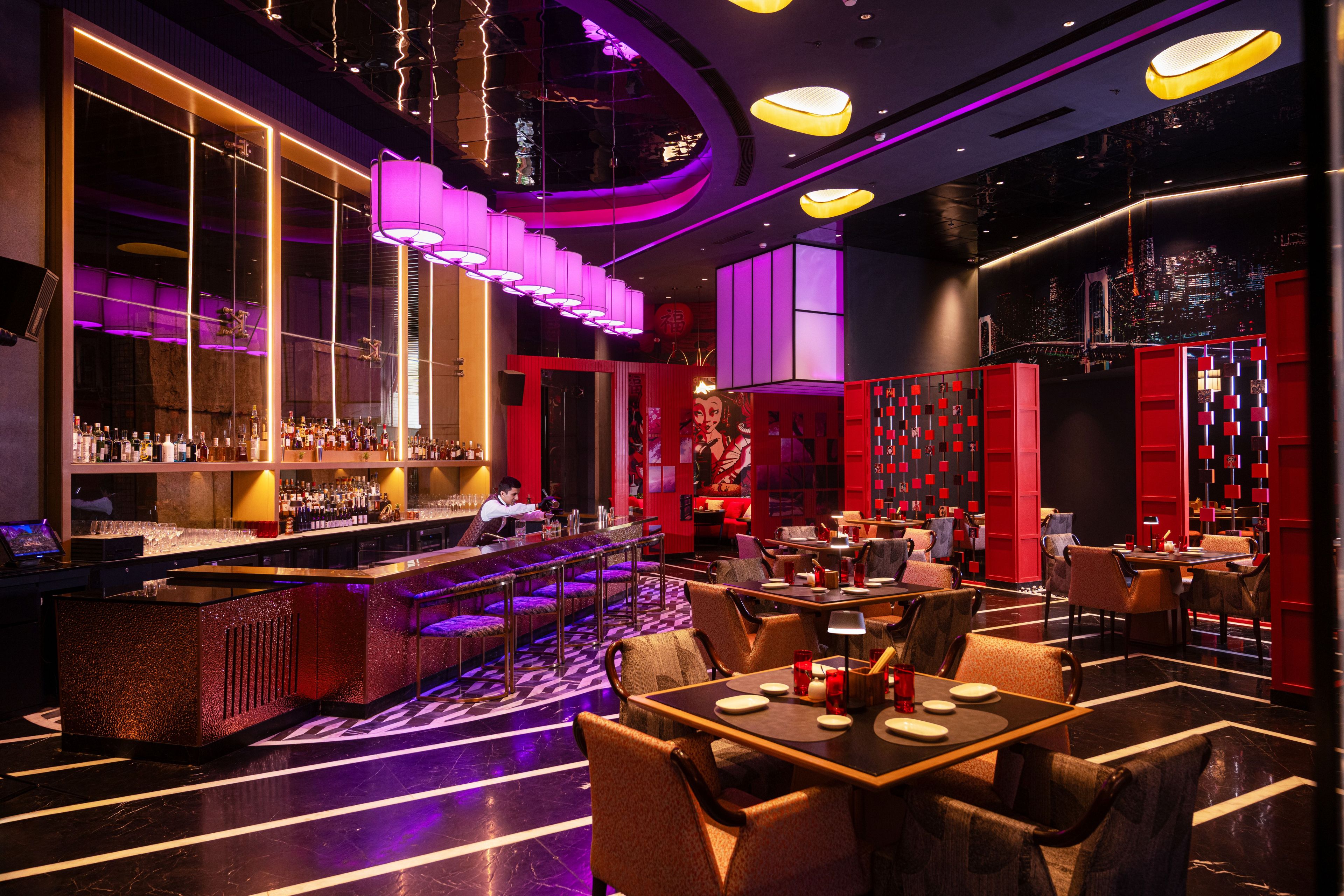 Uma área de bar moderna com um bartender, uma adega bem abastecida e um espaço de estar com mesas e cadeiras.