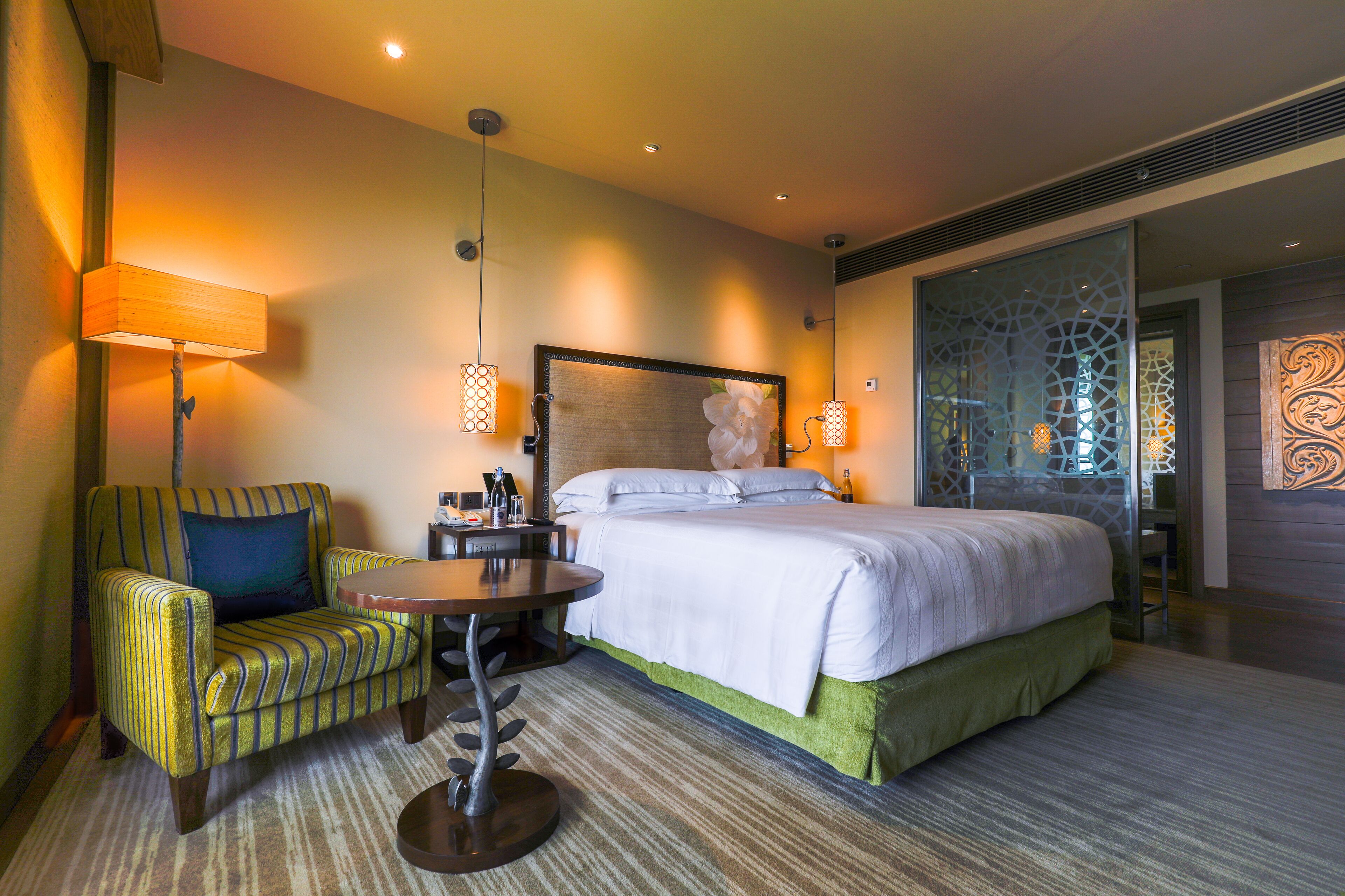 Una habitación de hotel con una cama, una silla, una mesita y una lámpara.