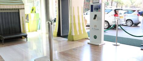 Un vestíbulo de hotel con mostrador de recepción, quiosco de autoservicio y estación de carga para vehículos eléctricos.