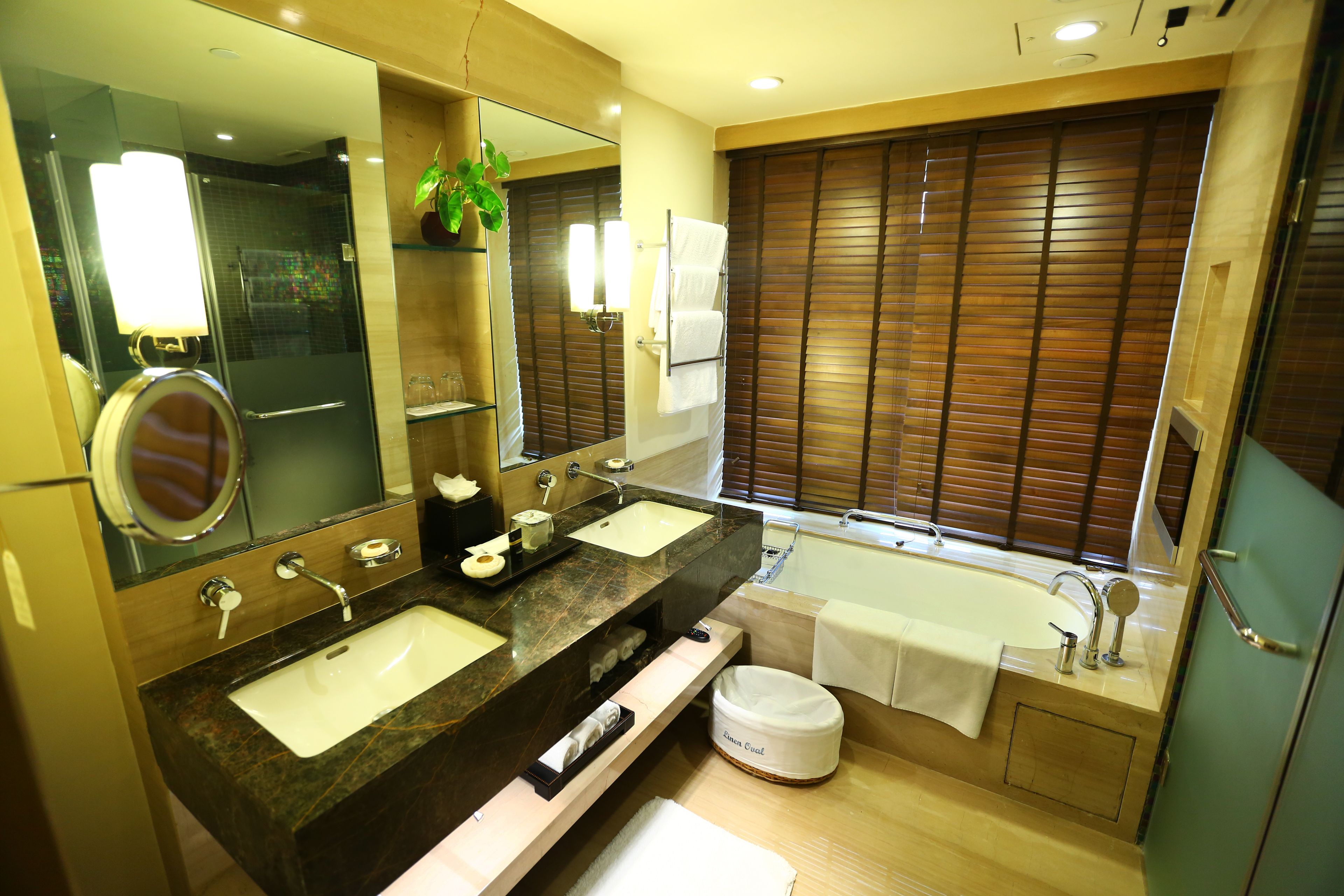 A modern bathroom with two sinks, a large mirror, a bathtub, and wooden blinds.