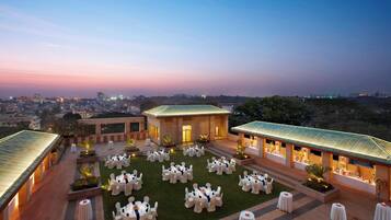 An outdoor event space with multiple round tables and chairs, surrounded by buildings with illuminated facades.