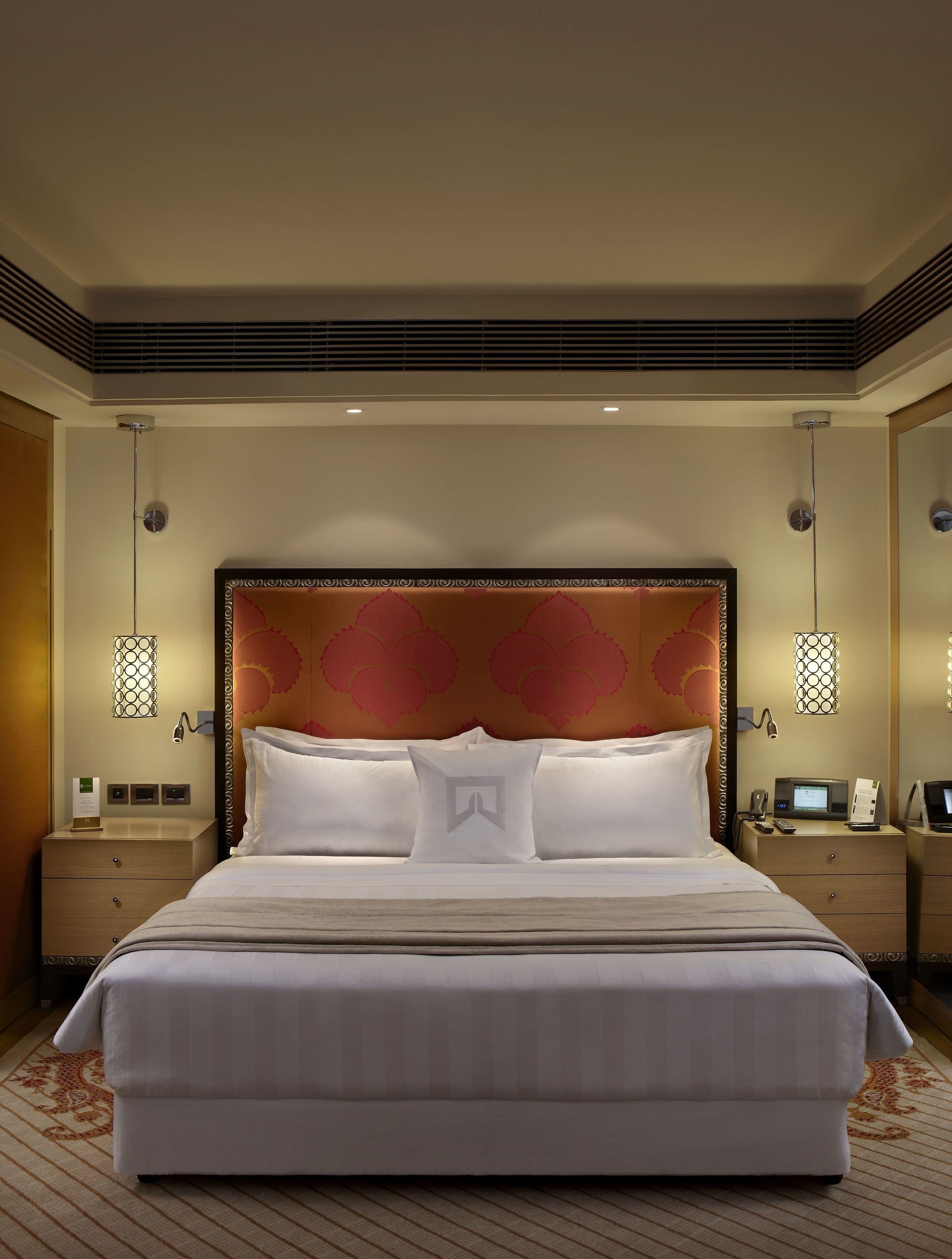 Una cama grande con cabecera decorativa, mesitas de noche con lámparas y un televisor de pantalla plana.
