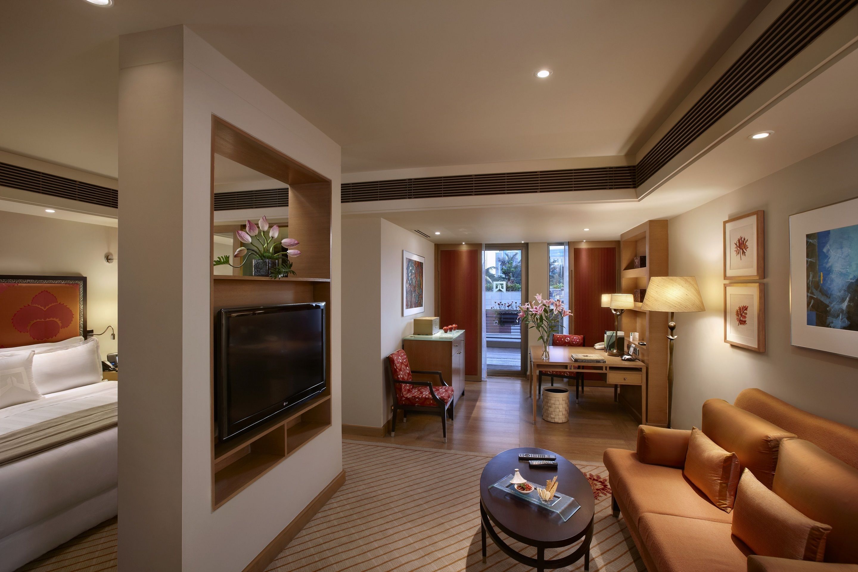 Habitación de hotel con televisor, sofá, mesa de comedor y vistas al exterior.