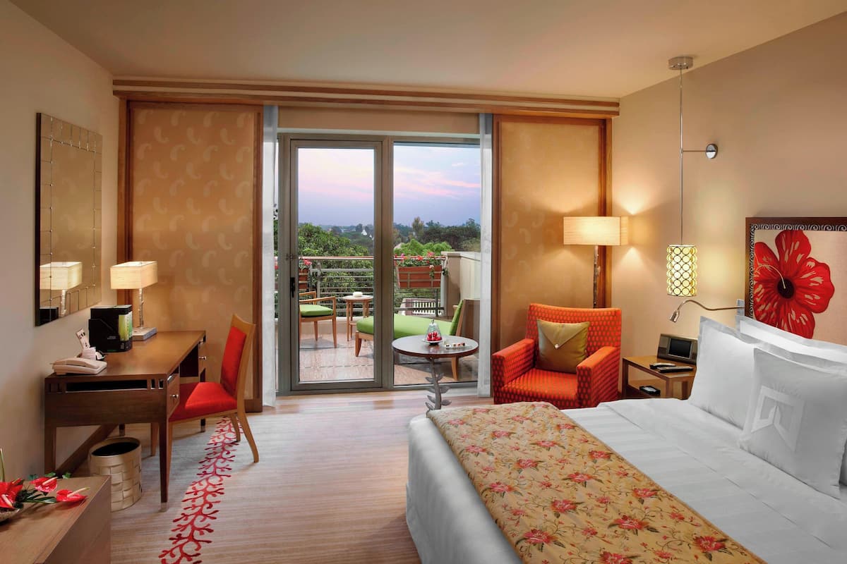 A hotel room with a bed, desk, chair, and a balcony with outdoor furniture.