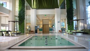 A spacious lobby with a central water feature, seating areas, and a reception desk.