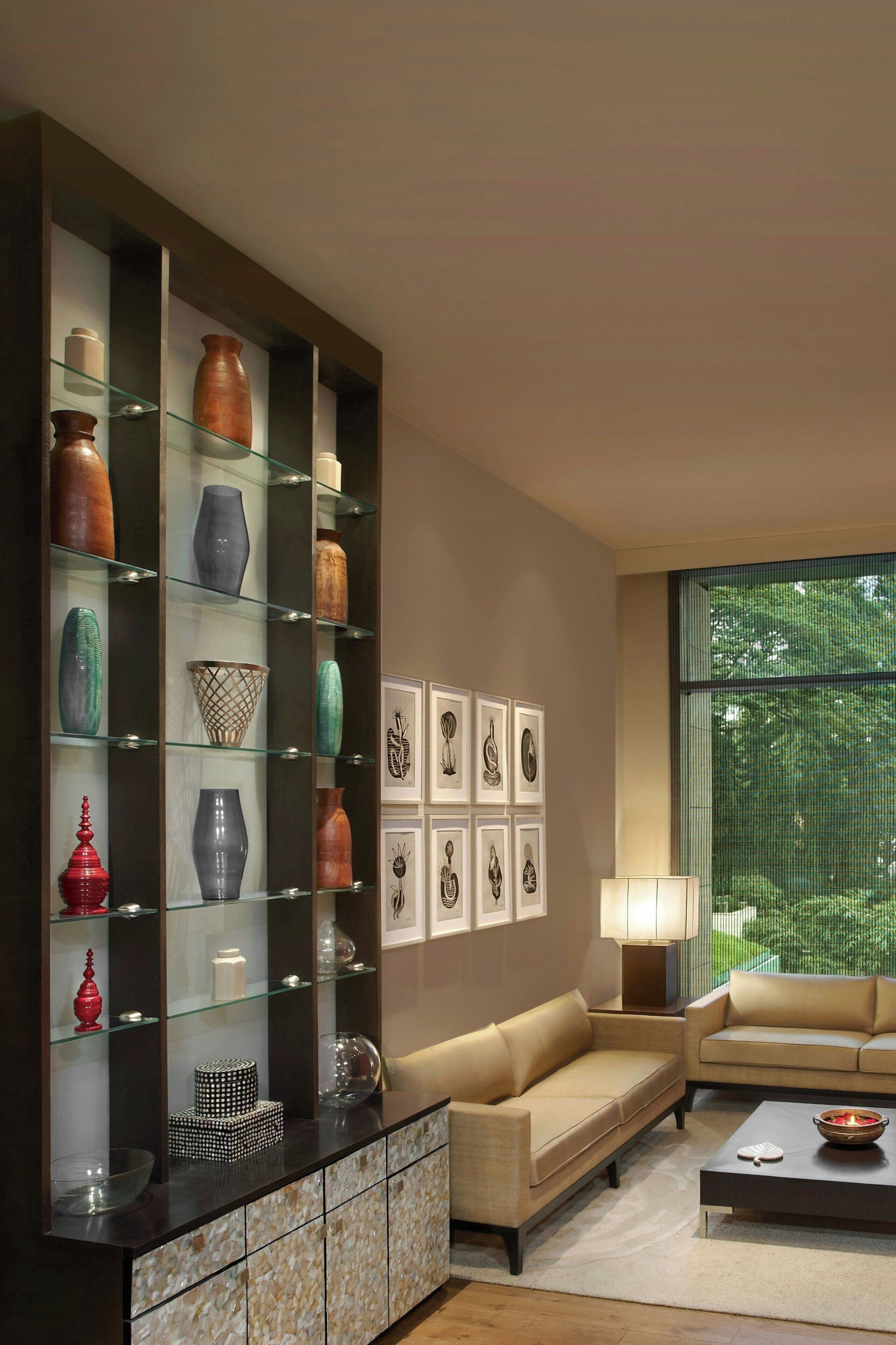A modern living room with a glass display cabinet filled with decorative items, a beige sofa, a coffee table, and framed artwork on the wall.