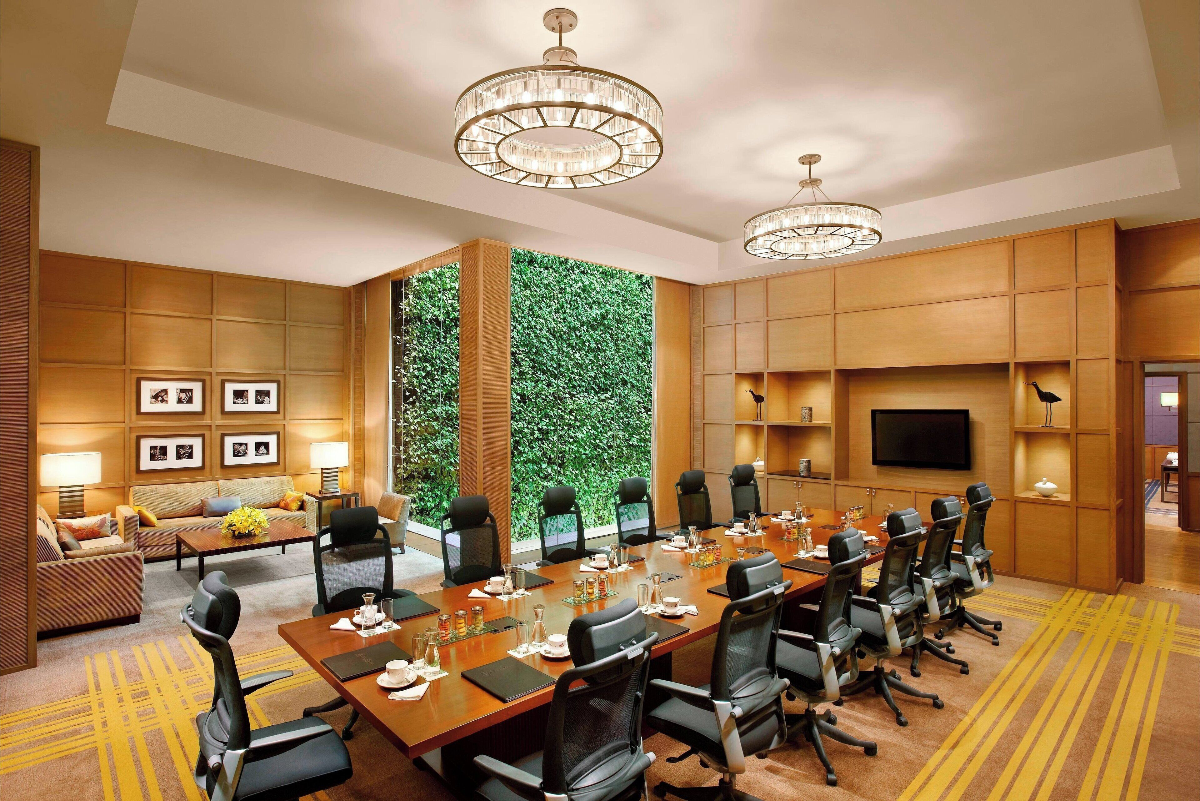 A conference room with a long table, chairs, a television, and a green wall.