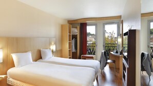 Quarto de hotel com duas camas, uma escrivaninha, uma cadeira, um guarda-roupa e varanda com vista.