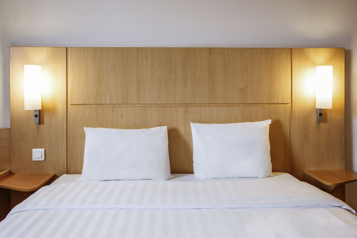 Habitación de hotel con cabecera de madera, dos almohadas blancas y lámparas de noche.