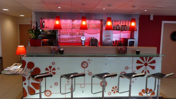 A bar area with a counter, stools, and a red-lit background. - ibis Etampes (Etampes)